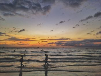 Silhouette people standing on beach against sky during sunset