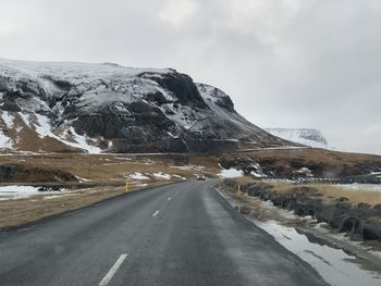 Road by snowcapped mountains against sky during winter