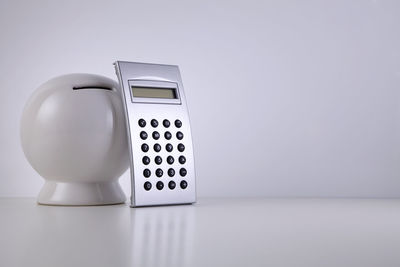 Close-up of piggy bank and calculator on table against white background