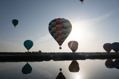 Hot air balloons flying over lake against sky