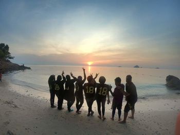 Group of people on beach against sky during sunset