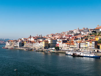 Cityscape by sea against clear blue sky
