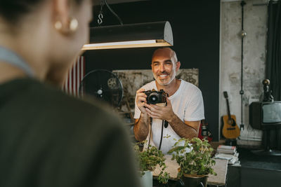 Happy male photographer holding digital camera while looking at colleague in studio