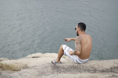 Full length of shirtless man using mobile phone in water