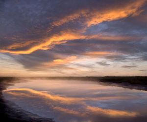 Scenic view of lake against dramatic sky during sunset