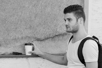 Portrait of young man drinking against wall