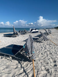 Deck chairs on beach against sky