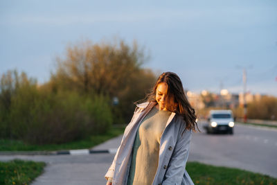 Beautiful smiling girl with long hair in a grey trench coat outdoors on the street spring