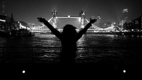 Silhouette woman with arms outstretched against illuminated tower bridge at night