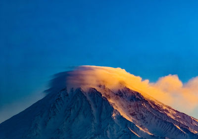 Smoke emitting from volcanic mountain against blue sky