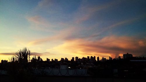 Silhouette of cityscape against cloudy sky