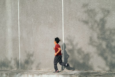 Full length of boy jogging against wall outdoors