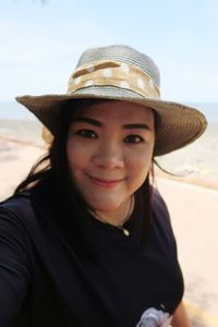 Close-up portrait of smiling mid adult woman wearing hat standing against sky during sunny day