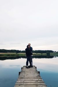 Couple standing on pier over lake against sky