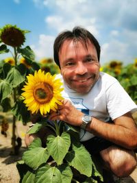 Portrait of smiling young woman with sunflower against plants