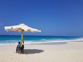 People on beach against clear blue sky