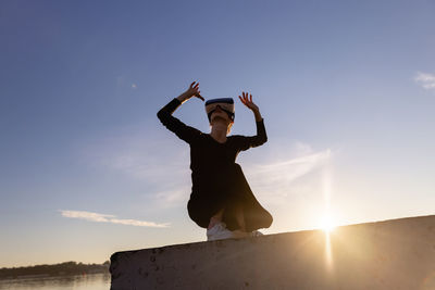 Rear view of woman with arms raised standing against sky during sunset