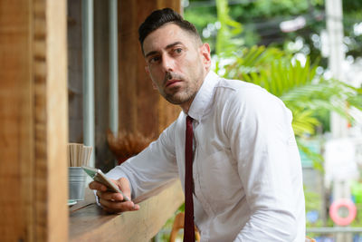 Young man holding camera while standing at cafe