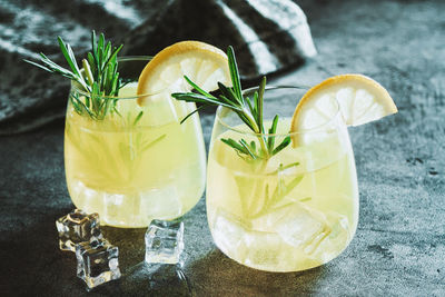 Cold cocktail, lemonade with lemon sliced, rosemary plant on dark concrete background. drink photo