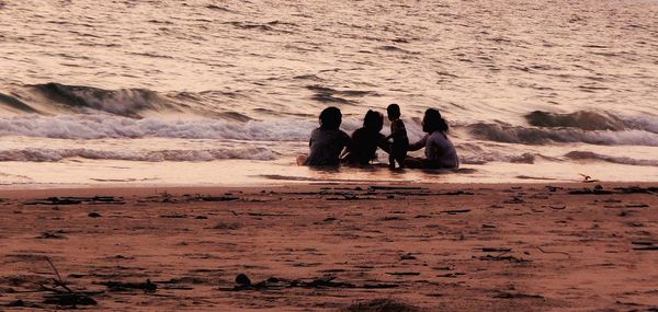 People enjoying in water at beach during sunset