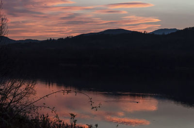 Scenic view of lake by silhouette mountains against orange sky