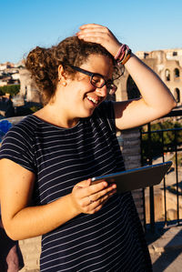 Beautiful young woman sitting on railing against sky