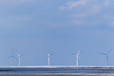 Wind turbines by sea against sky