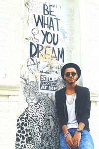 Full length of young man wearing sunglasses standing against wall