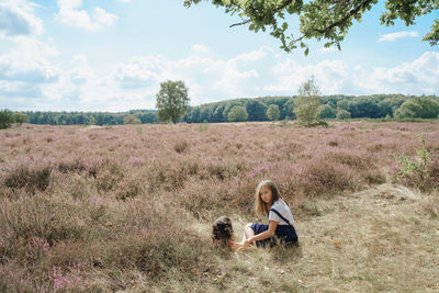 Rear view of girl sitting on grass in big field together with black dog