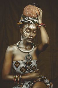 Close-up of  african woman sitting with pot on her head. covered in tribal bodyart