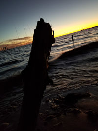 Silhouette wooden post on beach against sky during sunset