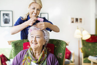 Happy female caretaker putting curlers to senior woman's hair at nursing home