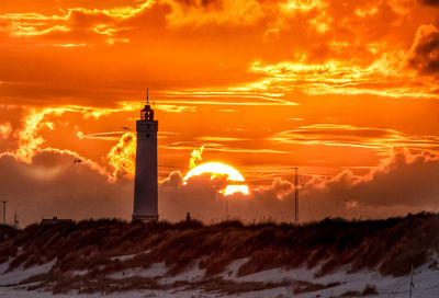 Lighthouse on street amidst buildings against sky during sunset