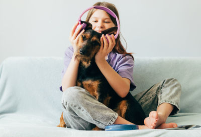 Girl with dog sitting on sofa at home