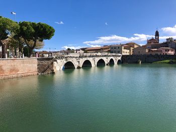 Arch bridge over river by buildings against sky