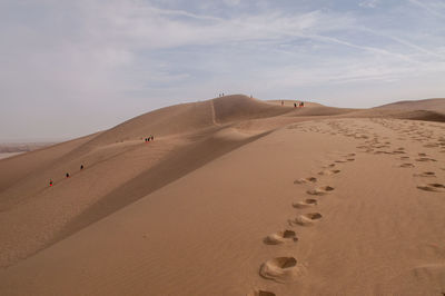 Footprints on sand dune in desert against sky