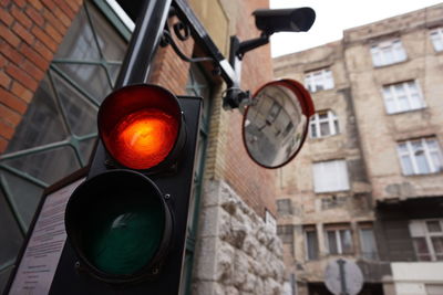 Low angle view of traffic signal with road mirror and security camera against buildings