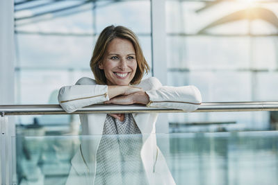 Happy businesswoman leaning on railing at the airport
