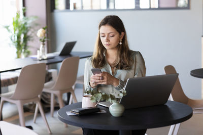 Young woman using phone while sitting on table