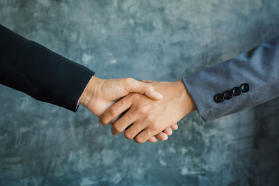 Cropped hands of businessmen shaking hands against wall