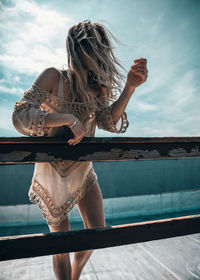 Woman leaning on railing against sky