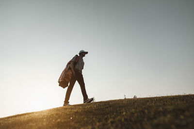 Low angle view of man walking on hill against clear sky