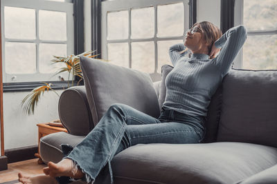 Side view of young woman sitting on sofa at home