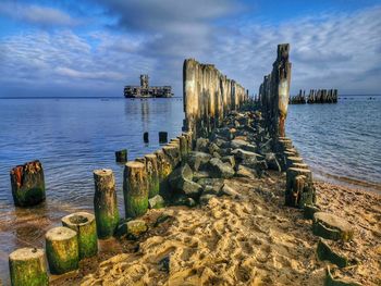 Wooden posts on beach by sea against sky