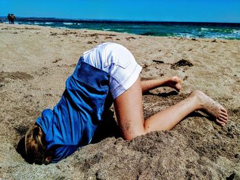 Midsection of woman lying on sand at beach against sky