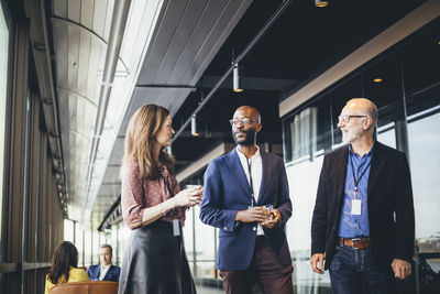 Female business person talking male coworkers in corridor at workplace