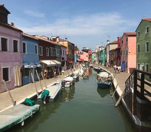 Boats moored in canal by buildings in city against sky