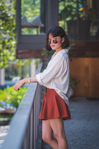 Portrait of young woman standing by railing in balcony