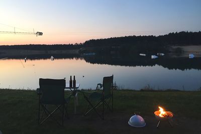 Fire in barbecue grill by lake against sky at dusk