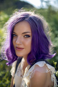 Portrait of a teenage girl with purple hair and an earring in her nose sit in the grass in nature